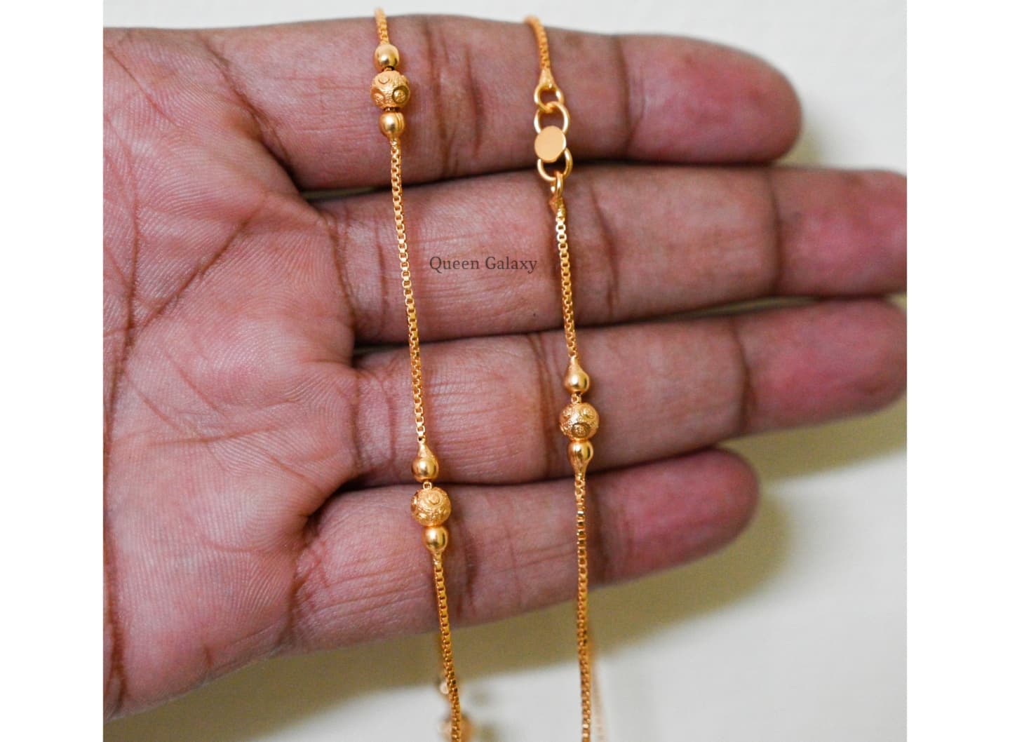 1 gram gold plated box ball anklet laid in a hand