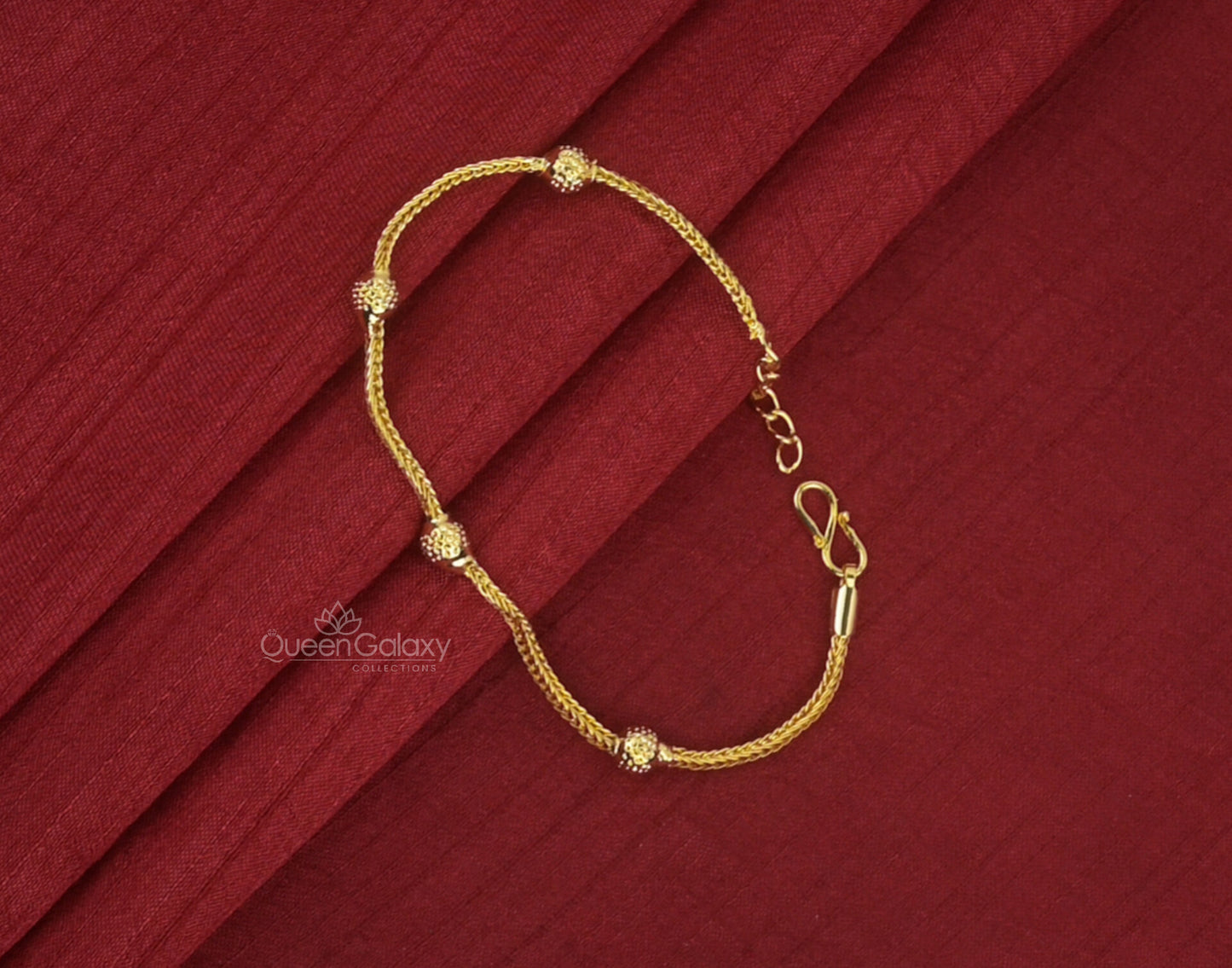 A gold plated bracelet with small spherical embellishments, displayed on a red fabric background.