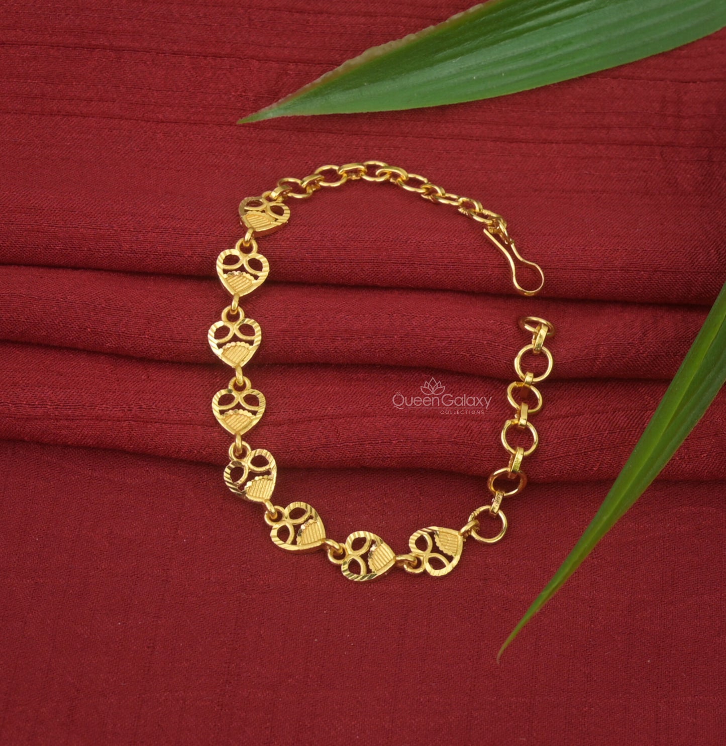 One Gram Gold Plated Heart Motif Bracelet with a link chain design displayed on a red fabric surface with a leaf beside it.