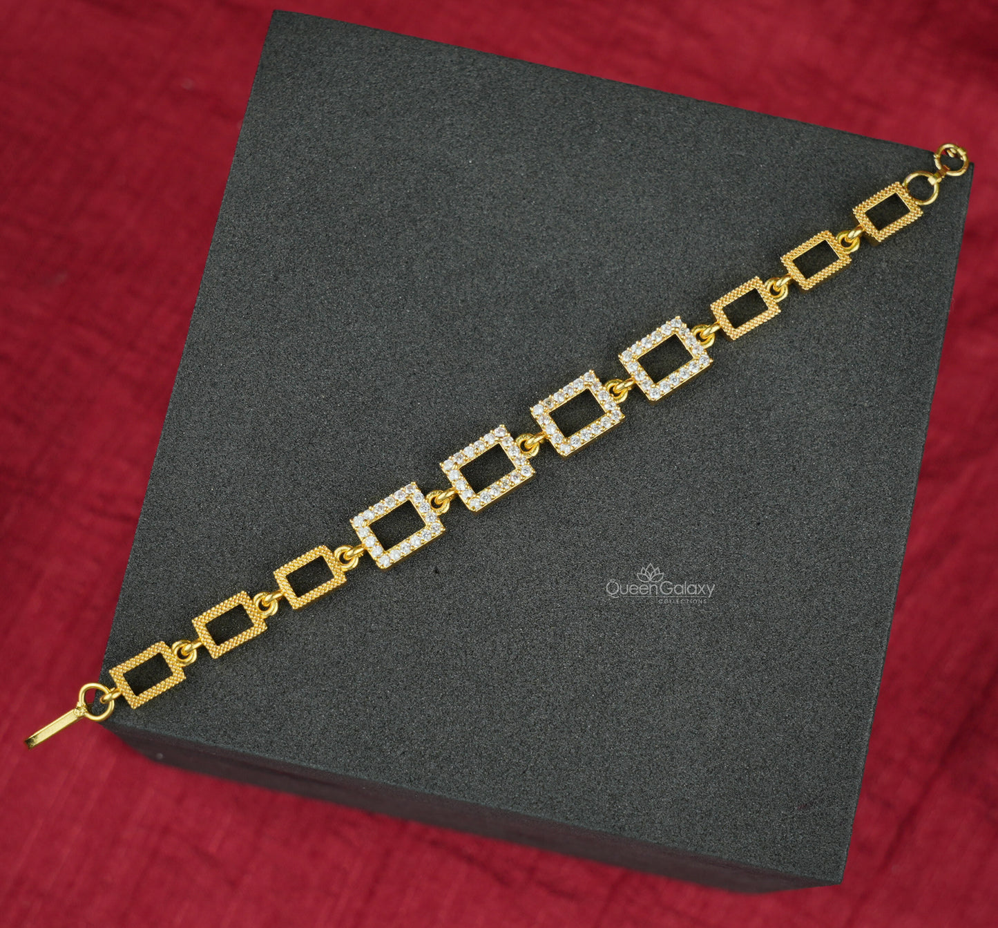 Gold Plated AD Stone Square Bracelet for Women displayed on a black platform with a red background.