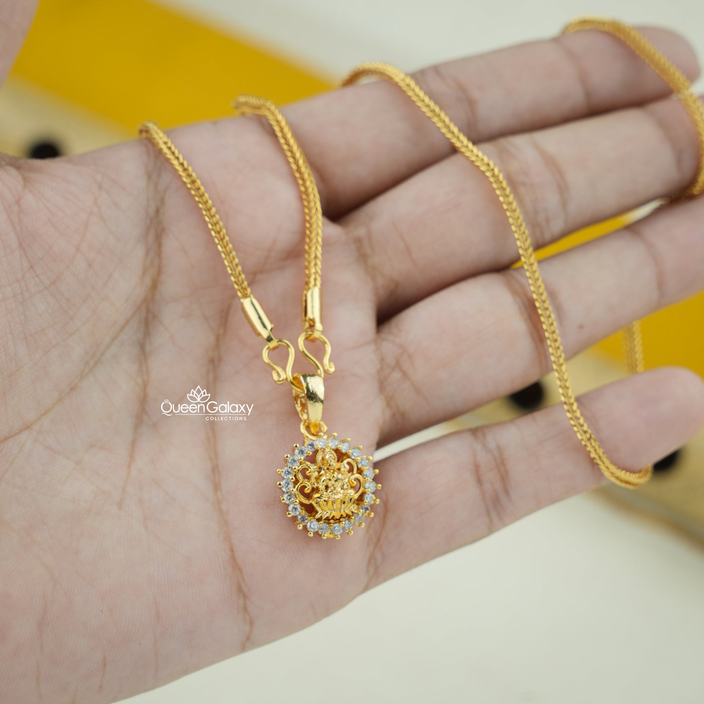 Gold plated chain with AD stone Lakshmi pendant on a hand against a yellow background at queen galaxy collection