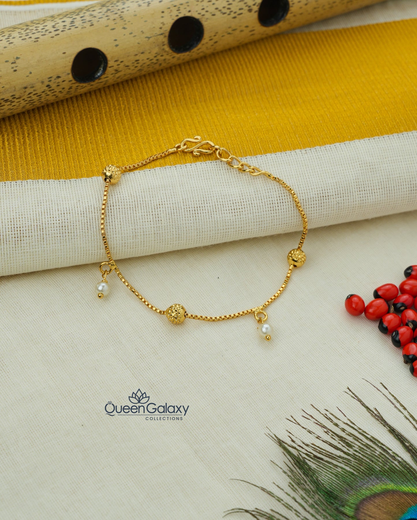 Gold Plated Bracelet with Pearl Drops & Beaded Charm laid out on a flat surface with a yellow fabric and decorative items in the background.