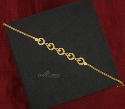 A gold plated bracelet with circular stone accents, displayed on a black platform with a red background.