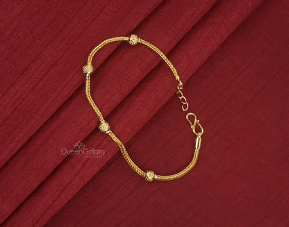 A gold plated bracelet with small spherical embellishments, displayed on a red fabric background.