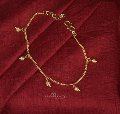Gold Plated Drop Charm Bracelet with small dangling embellishments, displayed on a red fabric surface.