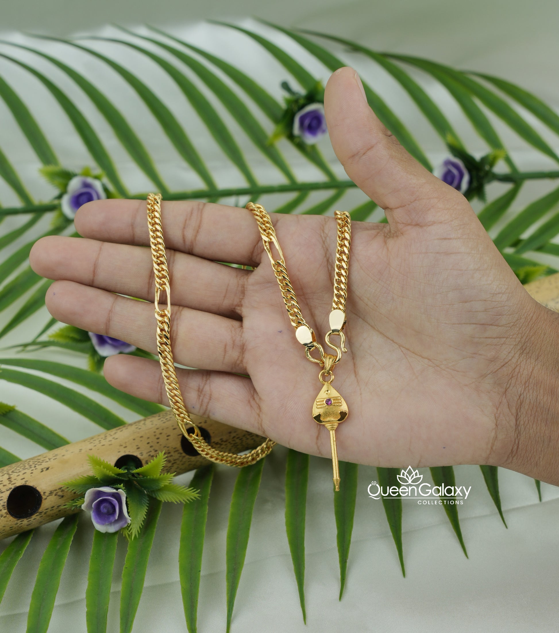 Gold plated Sahin chain with Murugan Vel pendant held by a hand with a green leafy background- queen galaxy collection