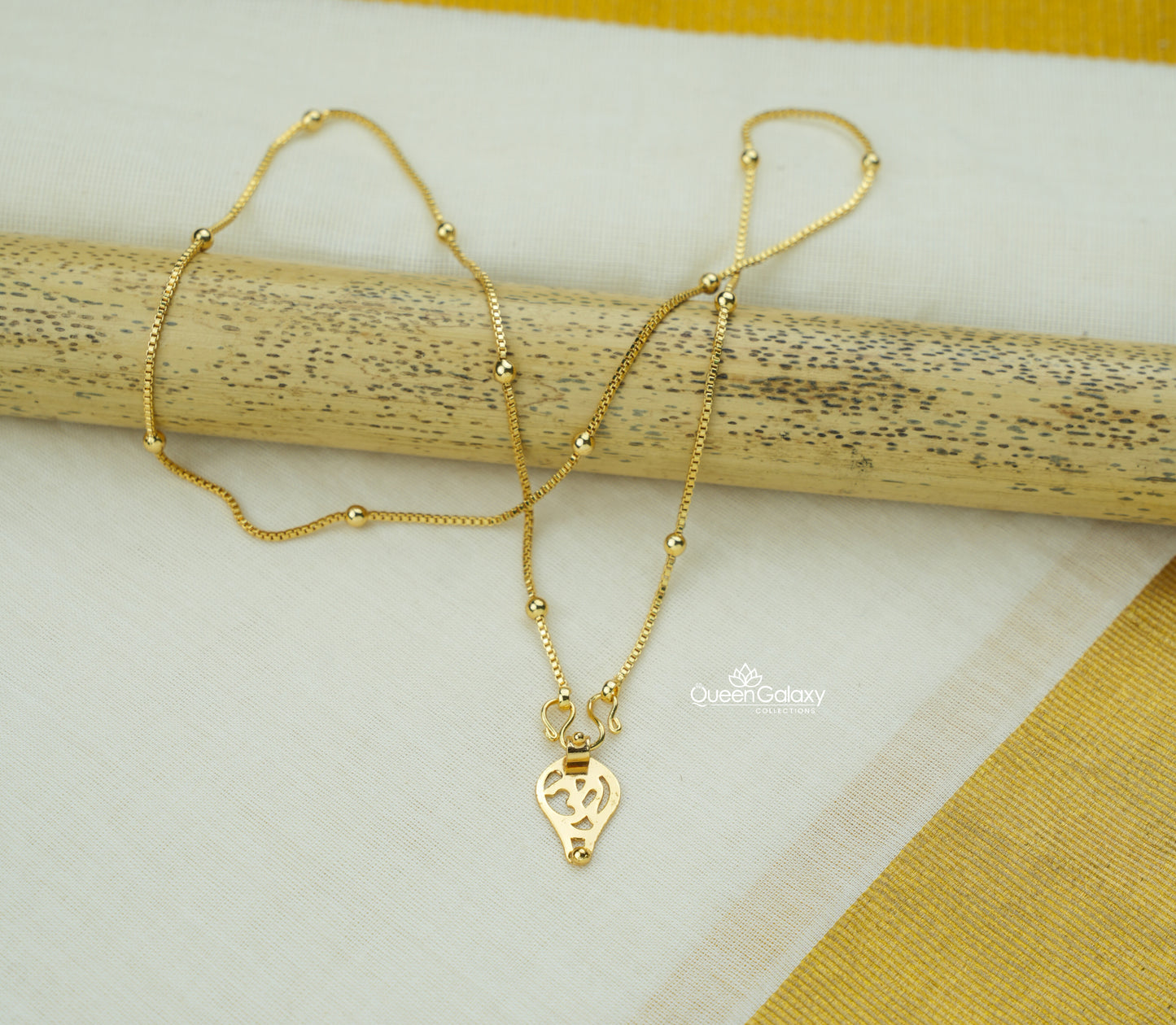 Gold Plated Hindu Thali Chain with Om Pendant on a wooden stick against a white and yellow fabric background