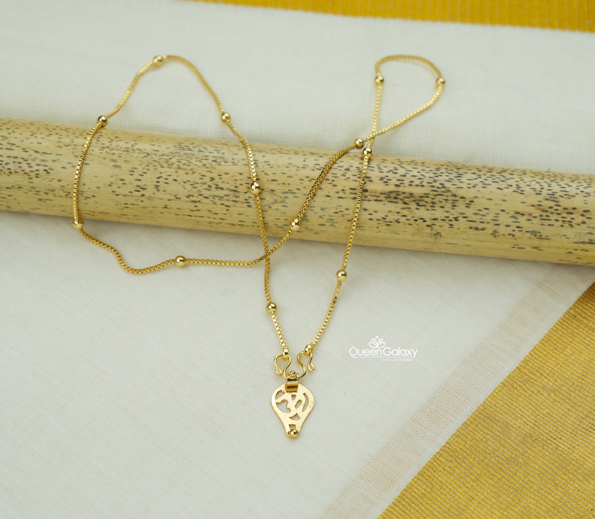 Gold Plated Hindu Thali Chain with Om Pendant on a wooden stick against a white and yellow fabric background