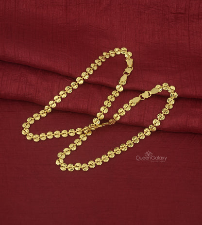 A gold-plated anklet laid out on a red fabric surface.