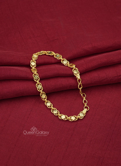 A gold plated crisscross chain bracelet with a patterned design, displayed on a red fabric surface at queen galaxy collections