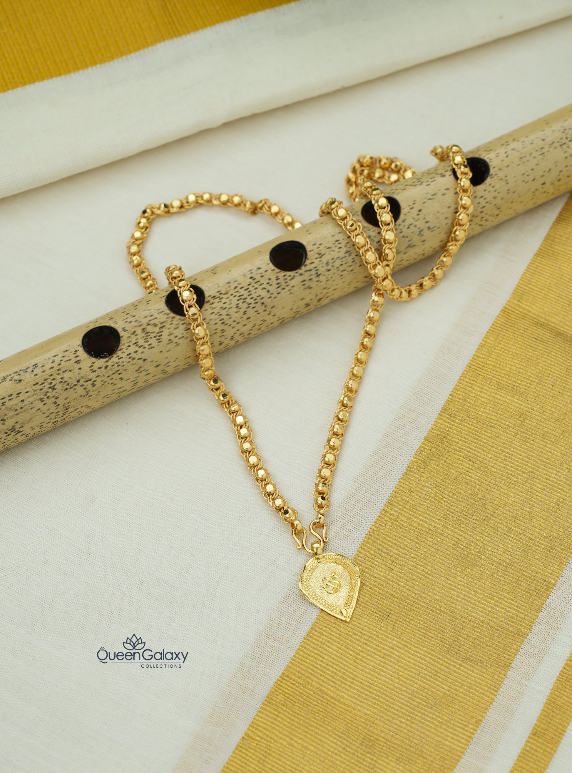 Gold plated chain with Om thali pendant placed on flute and kasavu saree background - queen galaxy collection