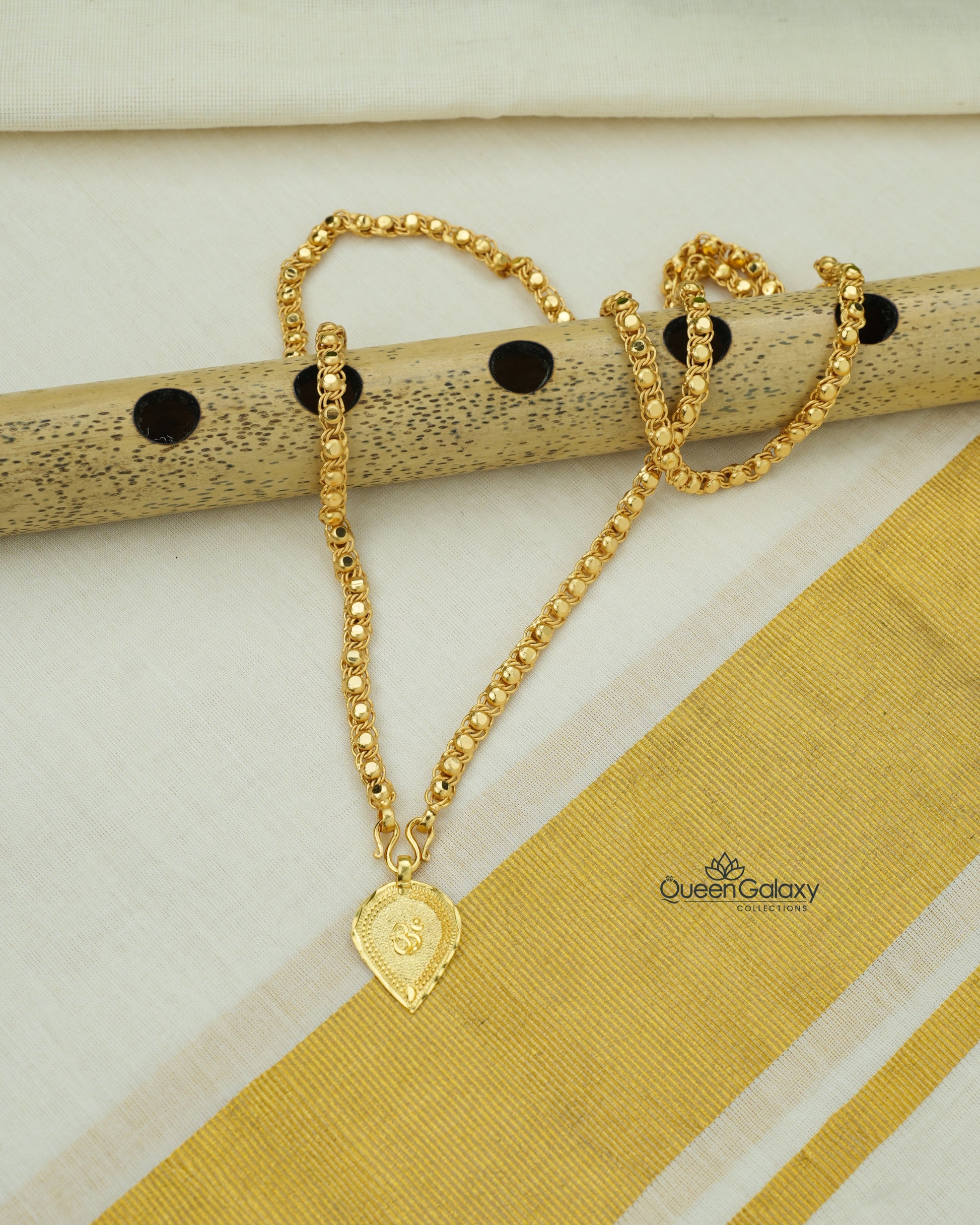 Gold plated chain with Om thali pendant placed on flute and kasavu saree background - queen galaxy collection