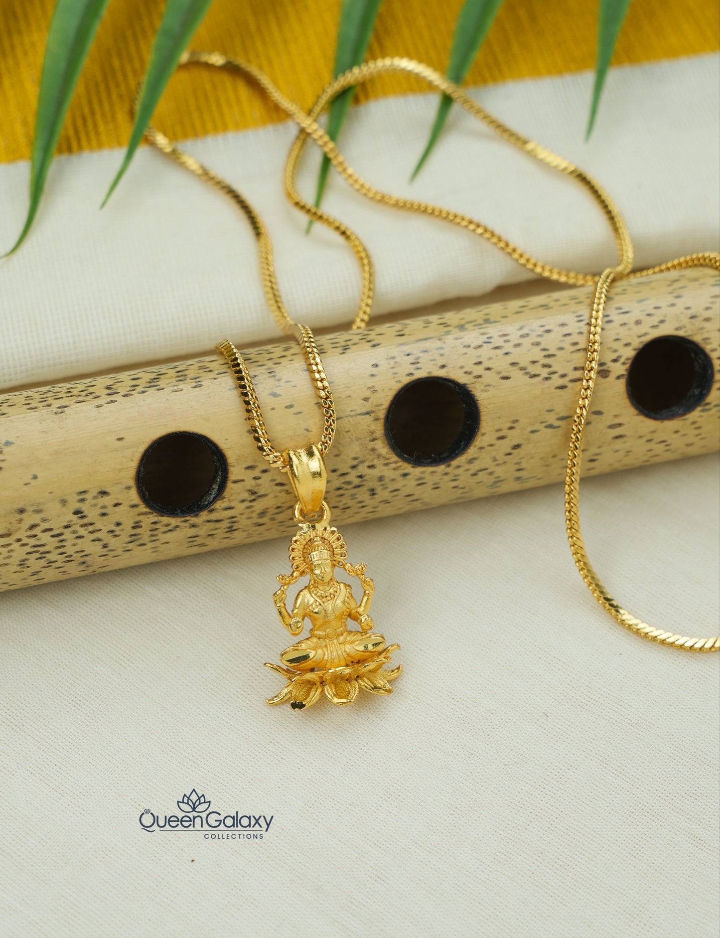 Gold plated box chain with Lakshmi Devi pendant on a white surface with a yellow fabric background- queen galaxy collection