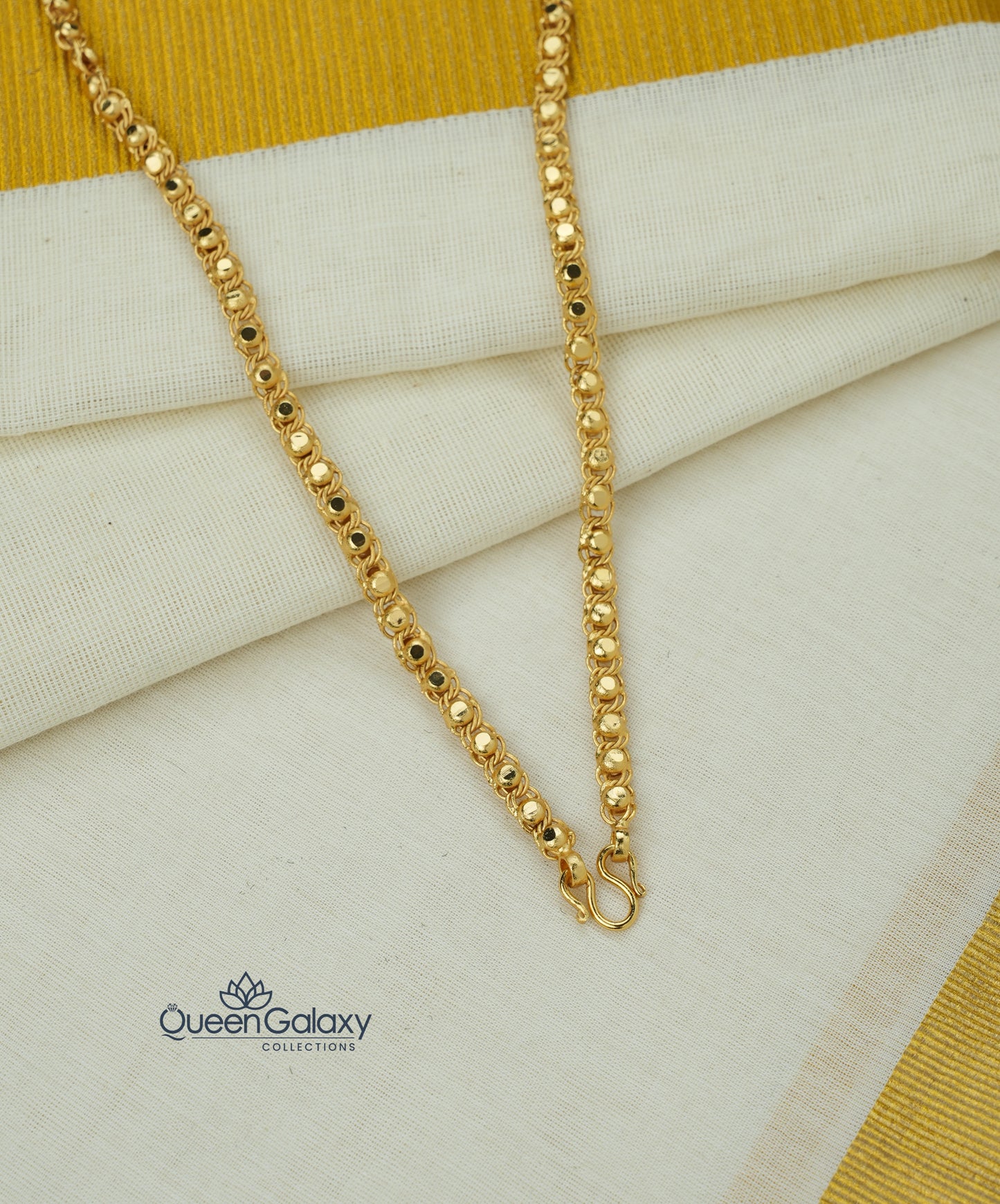 Gold plated designer chain roll on a fabric background with Queen Galaxy logo.